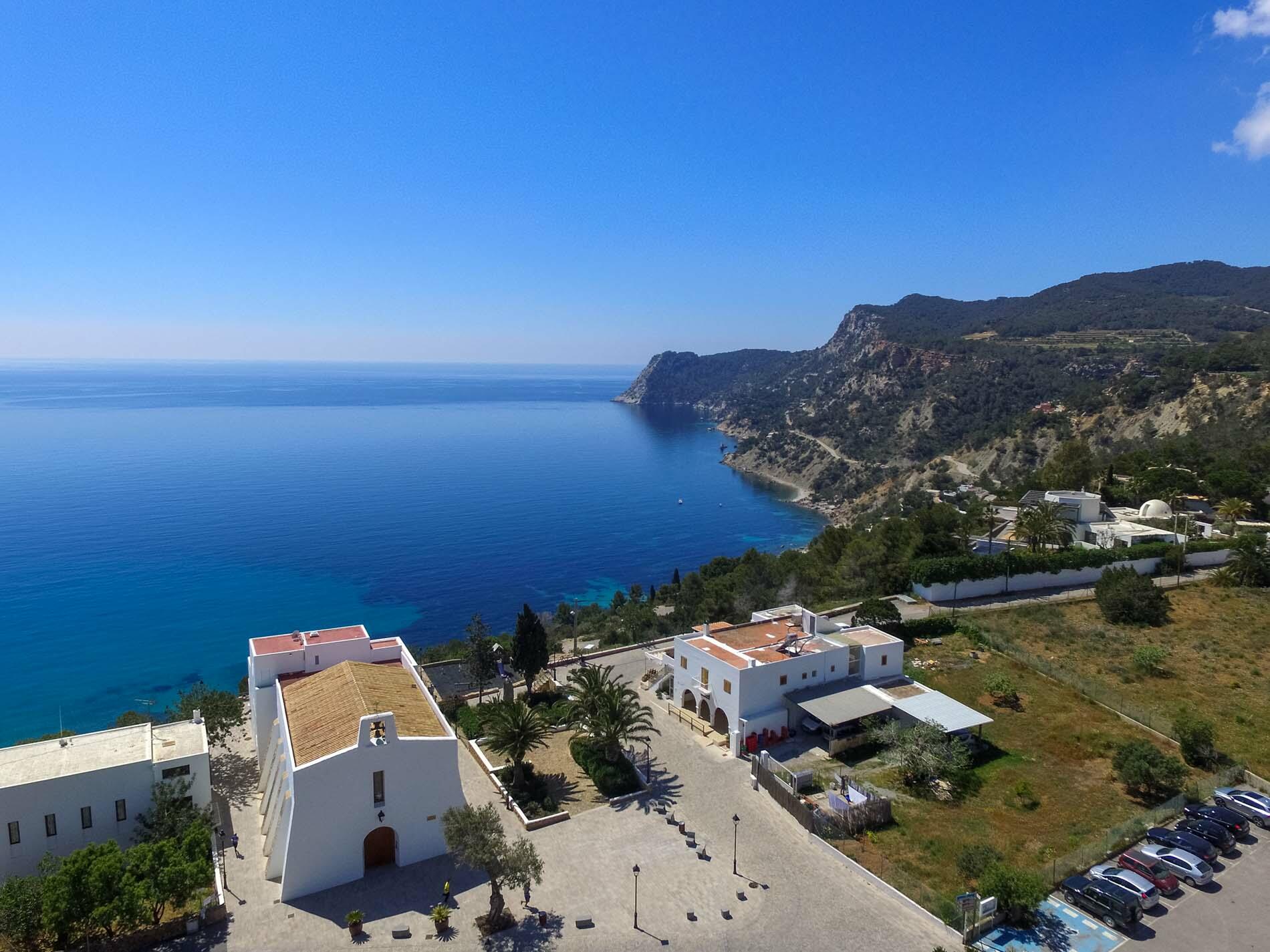 Vista elevada de Es Cubells, Ibiza, con una iglesia encalada que domina el mar azul y la escarpada costa
