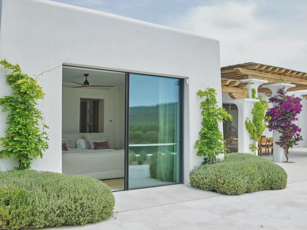 Villa Blakstad en Ibiza con paredes encaladas, puertas correderas de cristal, jardín paisajístico y terraza cubierta.